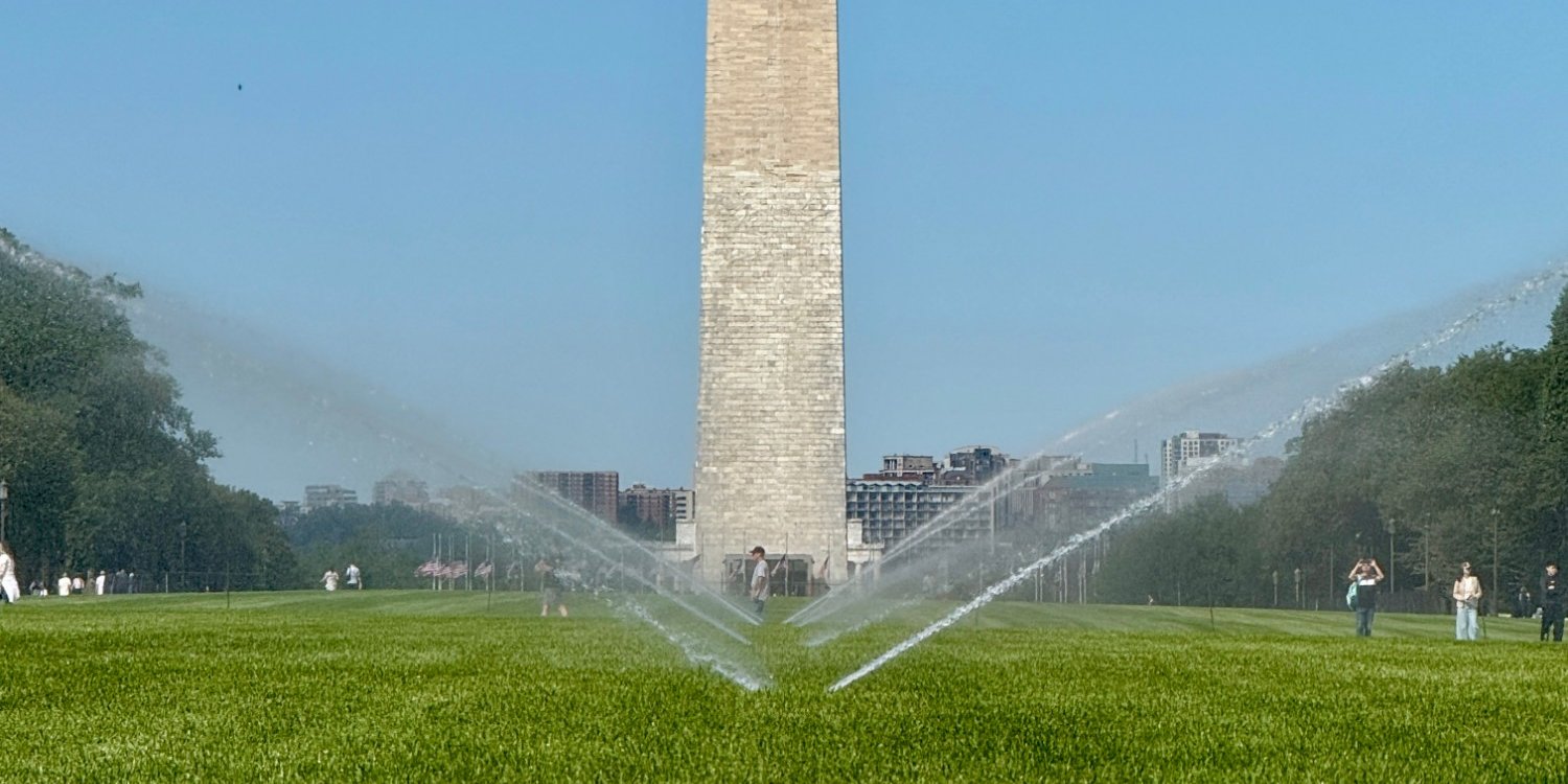 Sprinklers arcing over the National Mall lawn with the Washington Monument behind